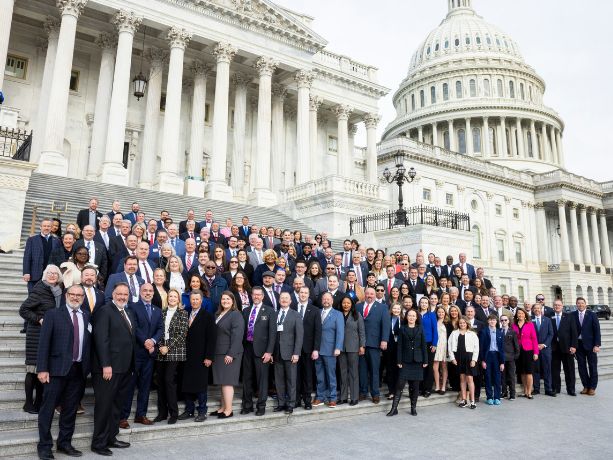 Members and state execs stand in front of the US Capitol.