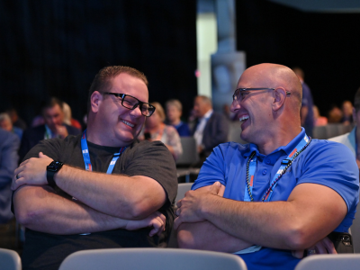 Two men in a conference audience smiling.